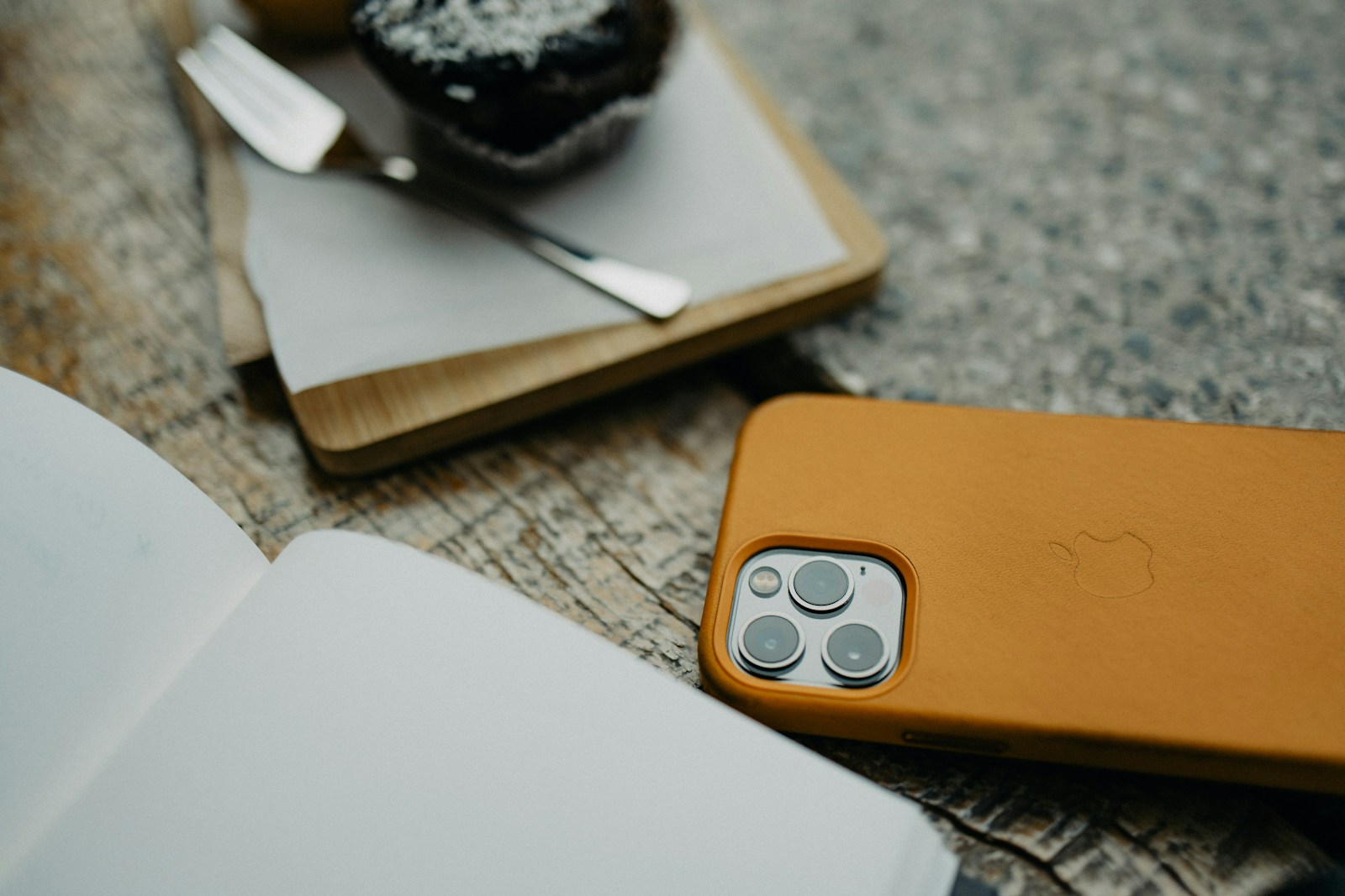 Smartphone met bruine hoes, notitieboek en muffin op houten tafel