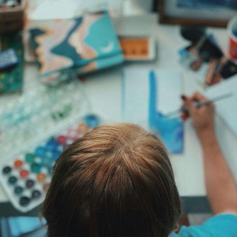 Kind schildert met waterverf aan bureau vol kunstbenodigdheden
